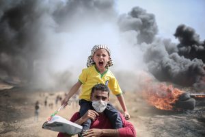 In questa immagine viene mostrata la fotografia di un bambino sulle spalle di un uomo che lo sta conducendo all'evacuazione. Sul suo viso si legge un grido agguerrito nei confronti della distruzione del suo Paese.