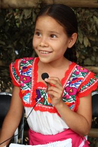 Nell'immagine viene rappresentata la foto di una ragazza indigena con un piccolo microfono in mano.